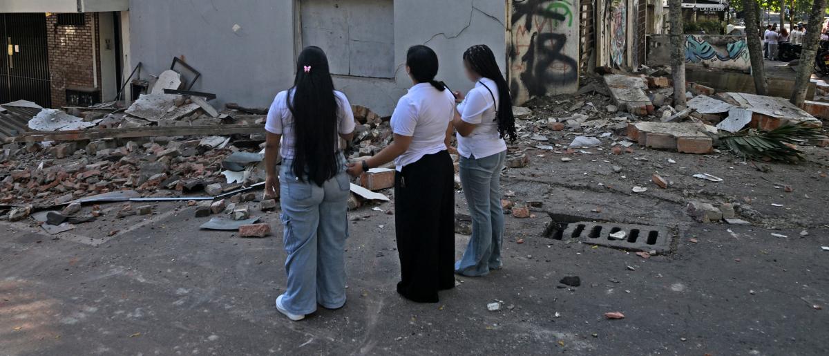 mujeres miran un edificio colapsado