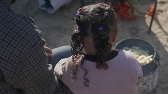 Una niña observa como un miembro de su familia cocina fuera de su tienda de campaña en el sur de Gaza.